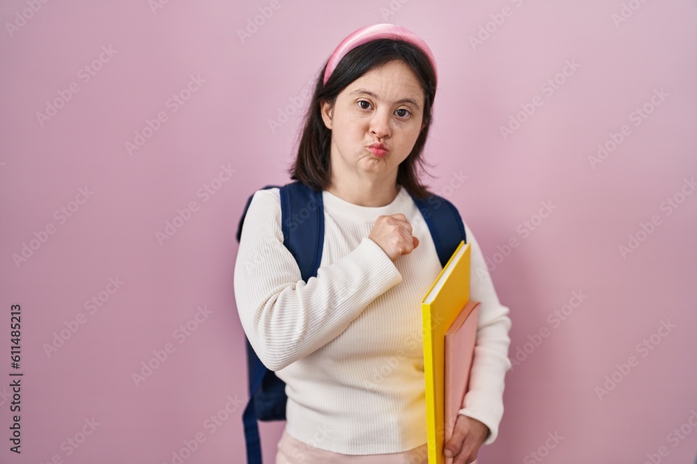 Woman with down syndrome wearing student backpack and holding books looking at the camera blowing a kiss on air being lovely and sexy. love expression. Woman with down syndrome wearing student backpack and holding books looking at the camera blowing a kiss on air being lovely and sexy. love expression.