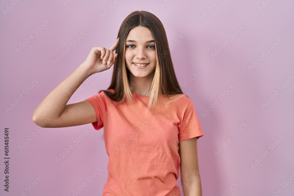 Fototapeta premium Teenager girl standing over pink background smiling pointing to head with one finger, great idea or thought, good memory