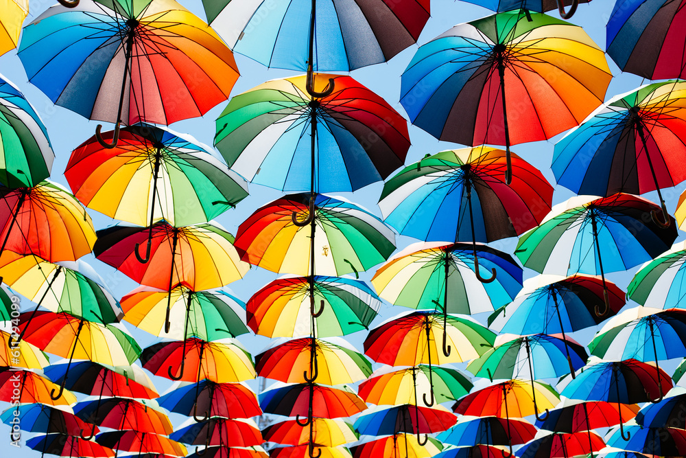 A lot of umbrellas coloring the sky in the city, a beautiful multi-colored texture, in bright sunlight.