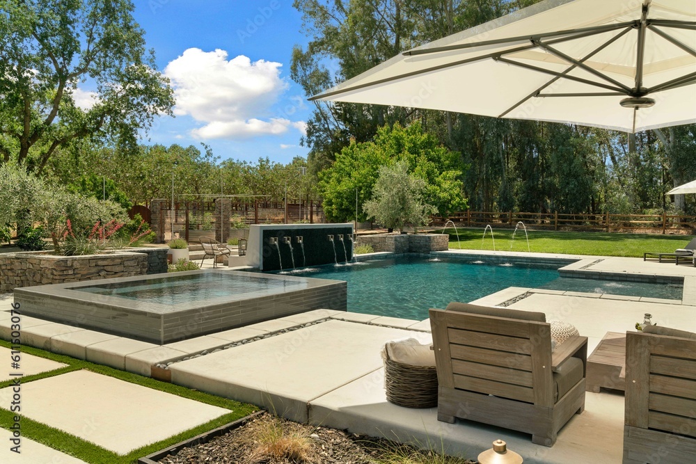 Side angle of a pool with a Jacuzzi surrounded by fountains and backyard furniture 