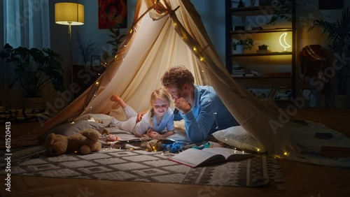 Young father and his kid daughter reading fairy tales while having fun in tent in living room photo