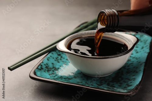 Fotografi Pouring soy sauce into bowl on grey table, closeup