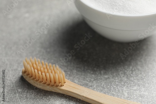 Bamboo toothbrush and bowl of baking soda on grey table, closeup