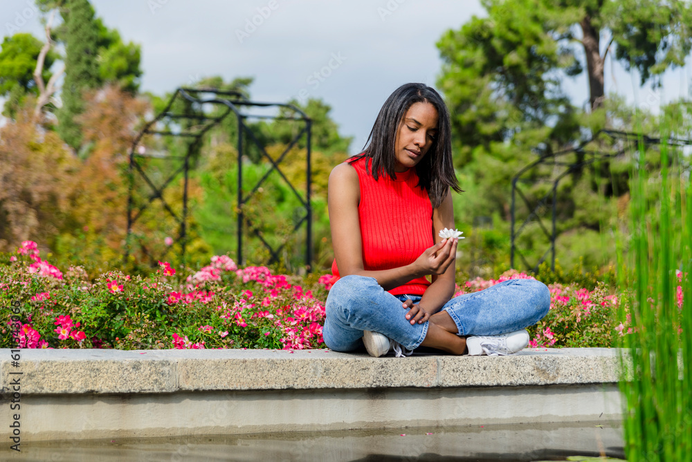 Naklejka premium Young mother thoughtful, with a flower outdoors in a park.