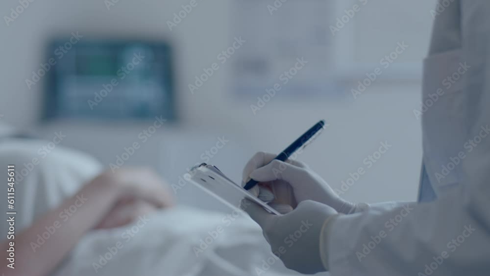Ill female patient in medical face mask lying on couch in a hospital ward, speaking with doctor as she taking notes during visit. Rack focus shot Ill female patient in medical face mask lying on couch in a hospital ward, speaking with doctor as she taking notes during visit. Rack focus shot