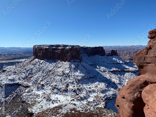  A stunning winter desert landscape featuring a snow-dusted, flat-topped mesa under a brilliant blue sky, showcasing the striking contrast between the white snow and red rock.