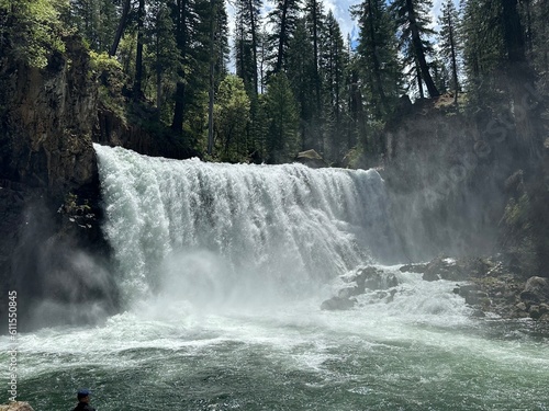 Wide waterfall plunging over rocky ledges into a foamy pool, surrounded by evergreen forest under evening light in Oregon wilderness.
