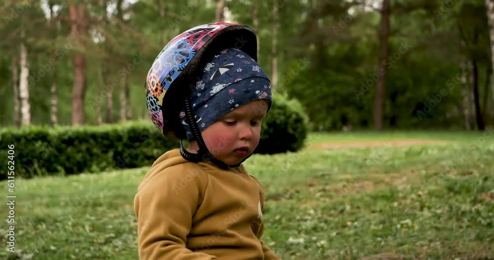 A child in a green park with a bicycle helmet on his head. Toddler two years old with a helmet on his head A child in a green park with a bicycle helmet on his head. Toddler two years old with a helmet on his head