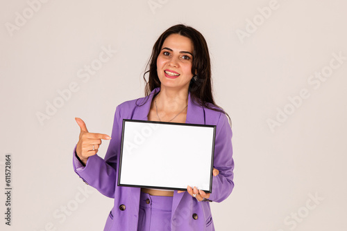 Beautiful young woman holding and pointing finger at empty blank white board, your text here concept. Smile Business woman portrait with blank white banner