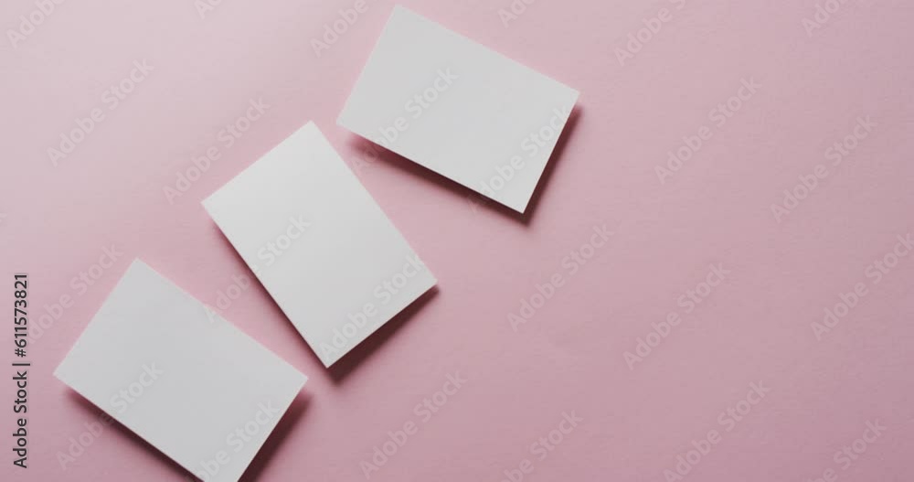 Overhead view of three white business cards arranged on pink background, copy space, slow motion