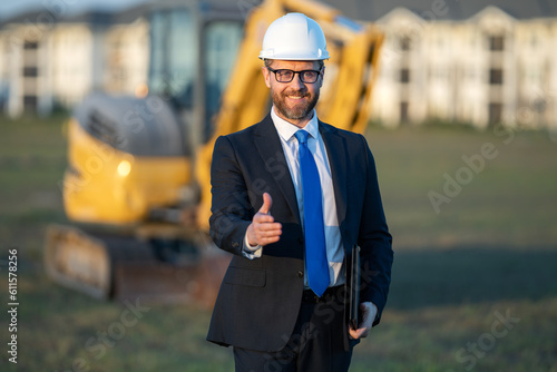 Construction builder investor. Man investor in front of construction site. Successful handsome man standing at modern home building construction. Portrait of midlle aged investor in suit and helmet.