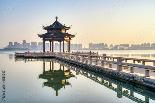 A pavilion and its reflection in the lake. Modern skyscrapers in distance. Photo is taken in Suzhou  Jiangsu province  China.