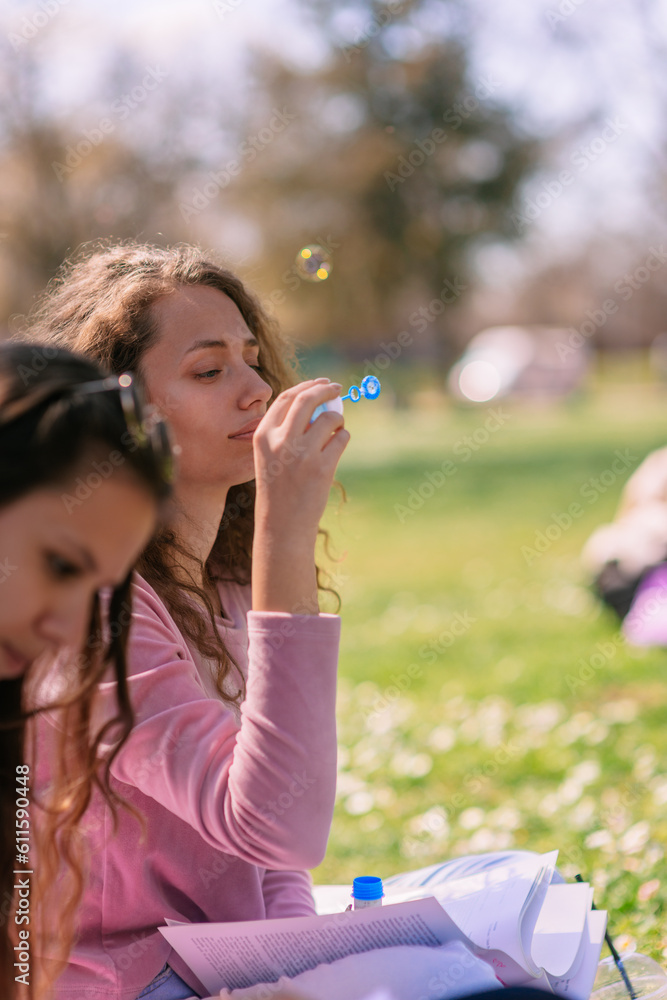 Curly haired girl blowing bubbles while her friend is studying for the exam at school Curly haired girl blowing bubbles while her friend is studying for the exam at school