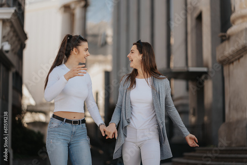 Photo of two happy young women enjoying a sunny day while strolling down a city street arm in arm