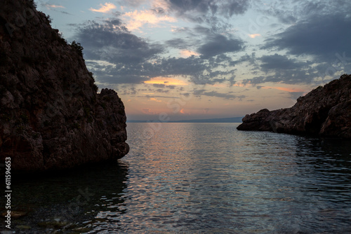 Tranquil Mediterranean shore with rocky cliff and sunset.