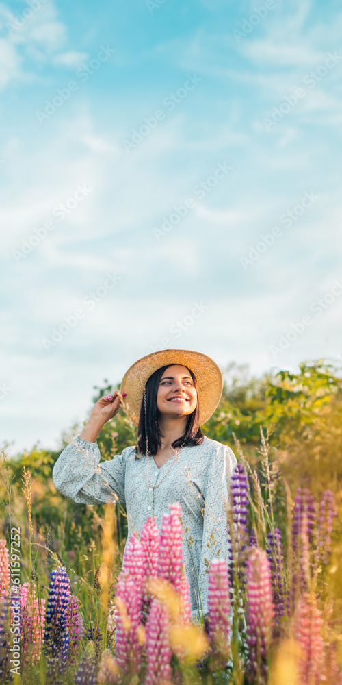 Portrait of young attractive woman in dress and straw hat on the summer meadow with blooming lupin flowers