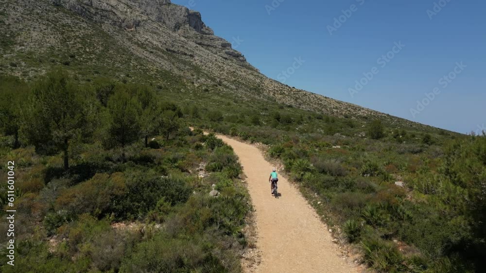 Outdoor cycling training.A female cyclist is riding her gravel bicycle on a gravel road between mountains.Gravel cycling adventure Outdoor cycling training.A female cyclist is riding her gravel bicycle on a gravel road between mountains.Gravel cycling adventure