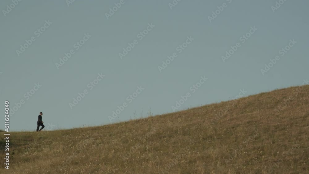 An adult man in a business suit walks to the top of the hill on the horizon against the blue sky An adult man in a business suit walks to the top of the hill on the horizon against the blue sky