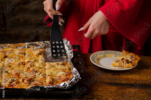 Unrecognizable girl takes piece of homemade pizza. Woman's hand with long nails holds kitchen spatula.