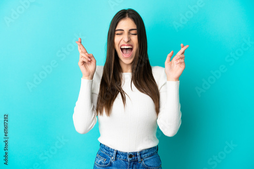 Young caucasian woman isolated on blue background with fingers crossing