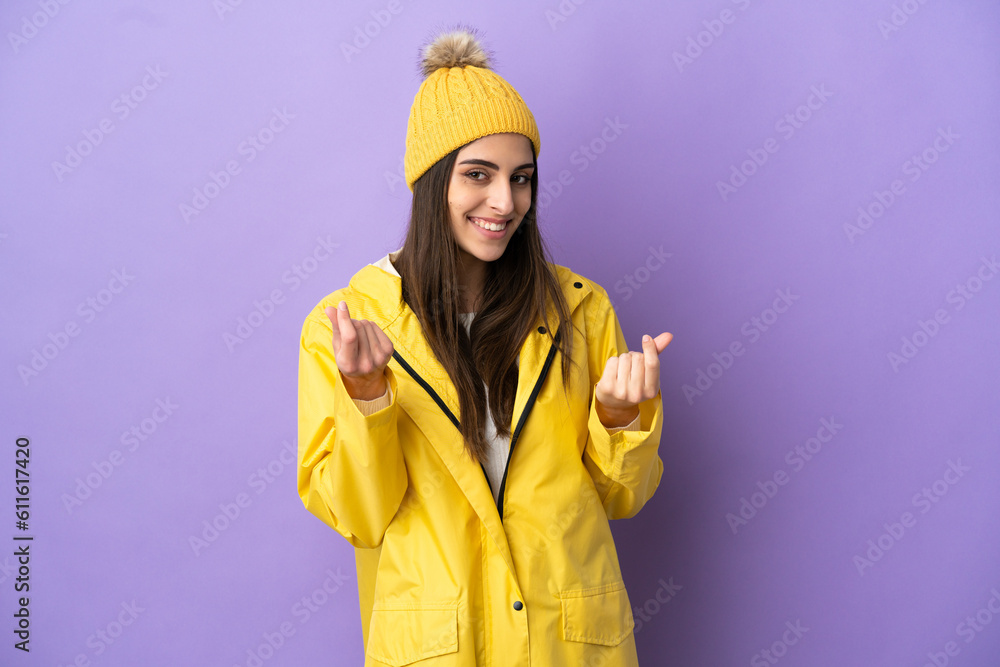 Young caucasian woman wearing a rainproof coat isolated on purple background making money gesture Young caucasian woman wearing a rainproof coat isolated on purple background making money gesture