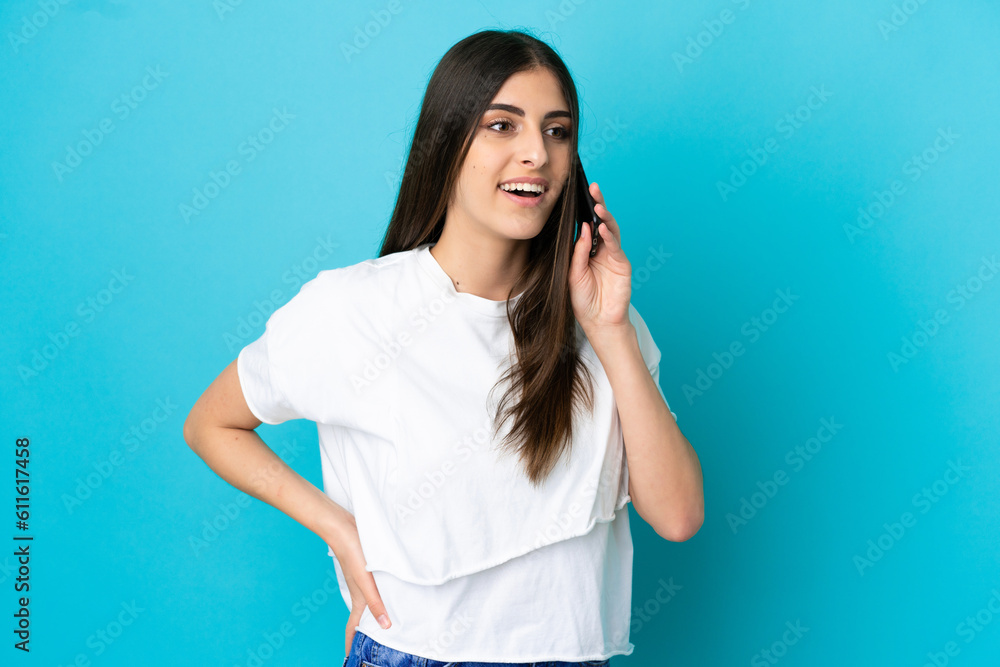 Young caucasian woman isolated on blue background keeping a conversation with the mobile phone with someone Young caucasian woman isolated on blue background keeping a conversation with the mobile phone with someone