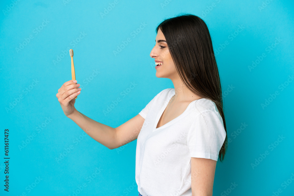 Young caucasian woman brushing teeth isolated on blue background with happy expression