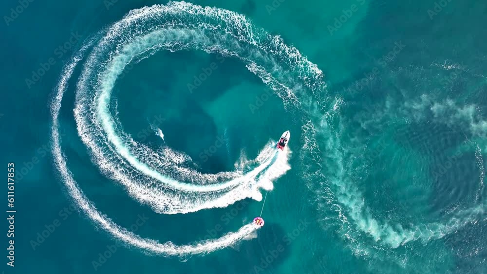 Tubing boat with people moving behind the boat on the water. Aerial view of motor speed boat