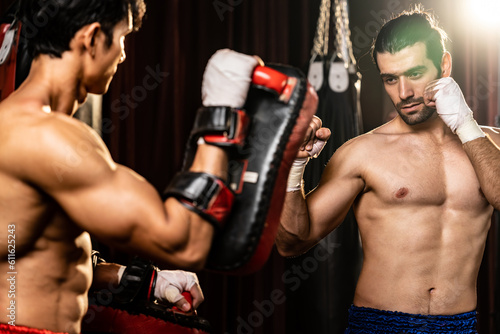 Asian and Caucasian Muay Thai boxer unleash punch in fierce boxing training session, delivering punching strike to sparring trainer, showcasing Muay Thai boxing technique and skill. Impetus photo