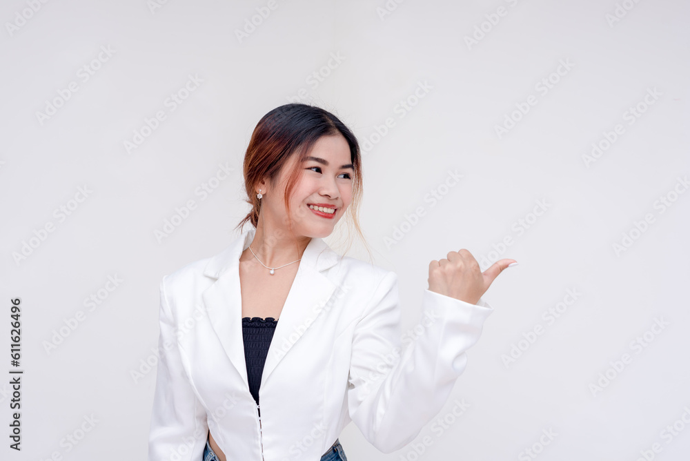 A smiling young woman looking sideways while gesturing to her right side with her thumb. Isolated on a white background. A smiling young woman looking sideways while gesturing to her right side with her thumb. Isolated on a white background.
