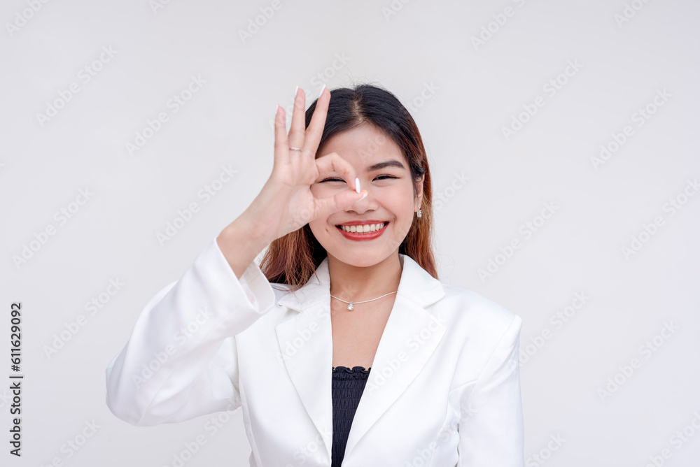 A happy young woman making okay gesture with her hand and peeking at it. Isolated on a white background. A happy young woman making okay gesture with her hand and peeking at it. Isolated on a white background.