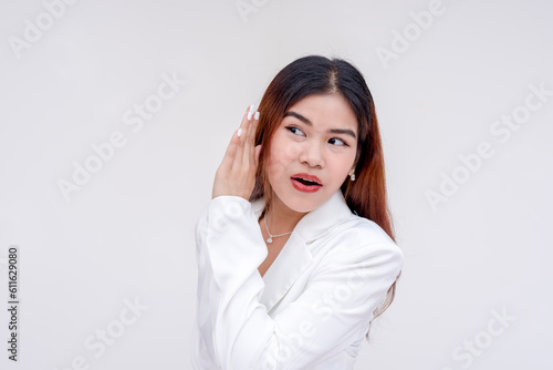 An intrigued young woman listening carefully with one hand on her ear. Isolated on a white background.