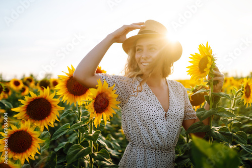 Beautiful woman posing in a field of sunflowers in a dress and hat. Fashion, lifestyle, travel and vacations concept.