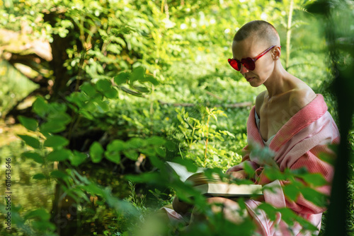Woman and reading a book outdoors. A bald woman in a bathrobe holds a book in her hands, sits on the green grass. Rest, recovery.