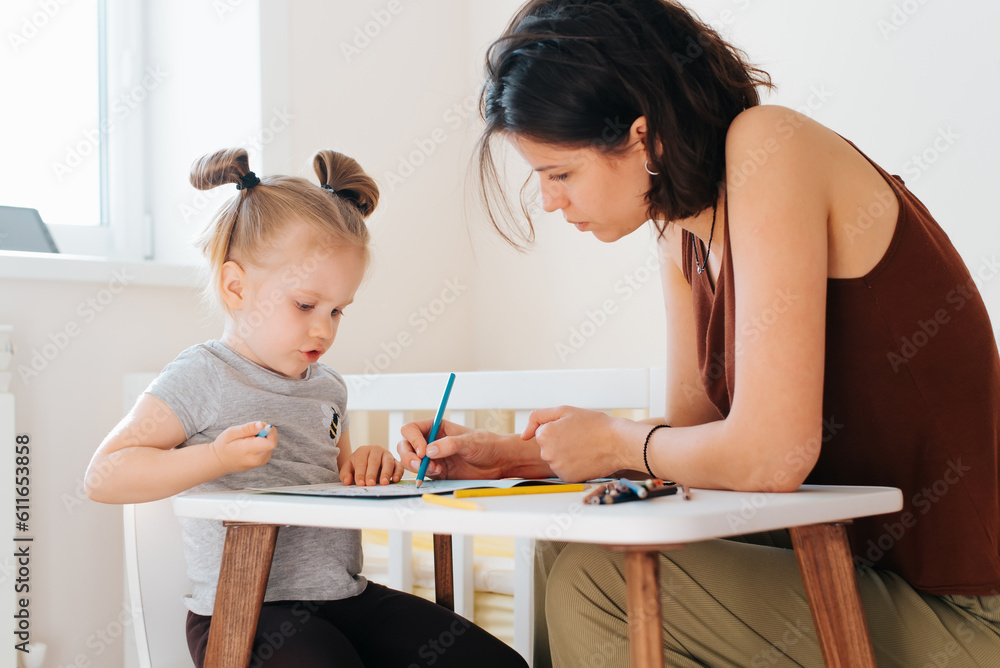 Mom and her beloved daughter drawing together with pencils in children's room, young mother teaching little girl paint drawing. Family education Mom and her beloved daughter drawing together with pencils in children's room, young mother teaching little girl paint drawing. Family education