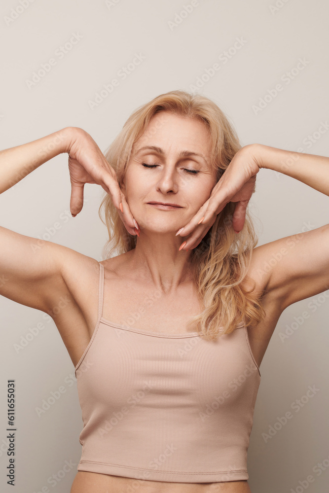 Beautiful blond middle aged woman smiling touching face closed eyes portrait. Elegant mature lady no makeup 50 years old close-up isolated on white Women's health, cosmetology, skin care Beautiful blond middle aged woman smiling touching face closed eyes portrait. Elegant mature lady no makeup 50 years old close-up isolated on white Women's health, cosmetology, skin care