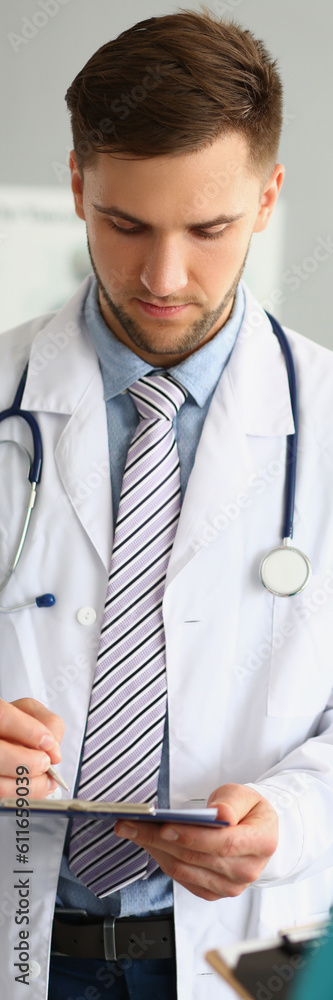 Fototapeta premium Male doctor filling out patient medical form in clinic. Medina contract and insurance concept