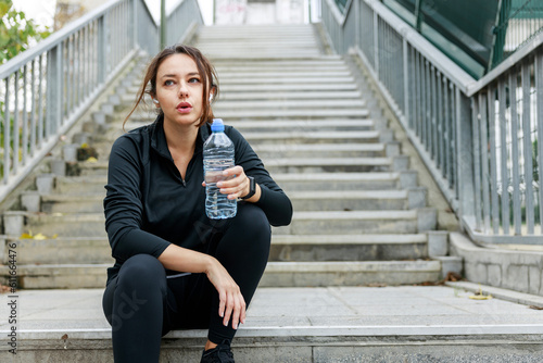 Young woman taking break jogging and drinking water from a bottle outdoor