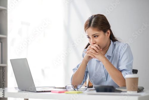 Puzzled confused asian woman thinking hard concerned about online problem solution looking at laptop screen, worried serious asian businesswoman focused on solving difficult work computer task photo