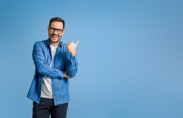 Portrait of cheerful businessman pointing at copy space for advertising against blue background