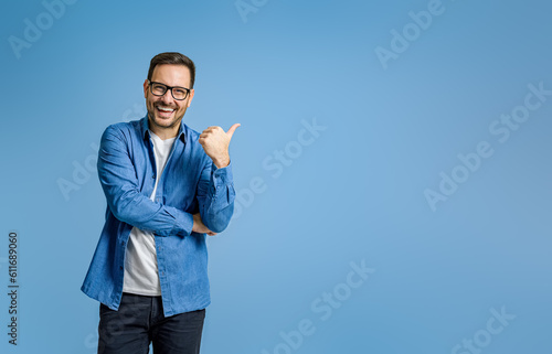 Portrait of cheerful businessman pointing at copy space for advertising against blue background photo