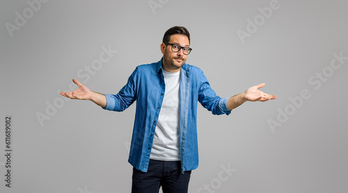 Confused businessman spreading hands and shrugging shoulders over gray background, I don't know