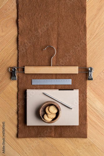 Pen, ruler, book, clothes hanger and a bowl of cookies on an elegant brown scarf on a wooden floor