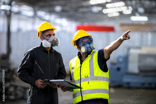 Two officers wearing gas masks, holding tablet and book, inspect the chemical spill site in an industrial warehouse to assess the damage, wearing gas masks, inspecting and evaluating toxicity of leak.
