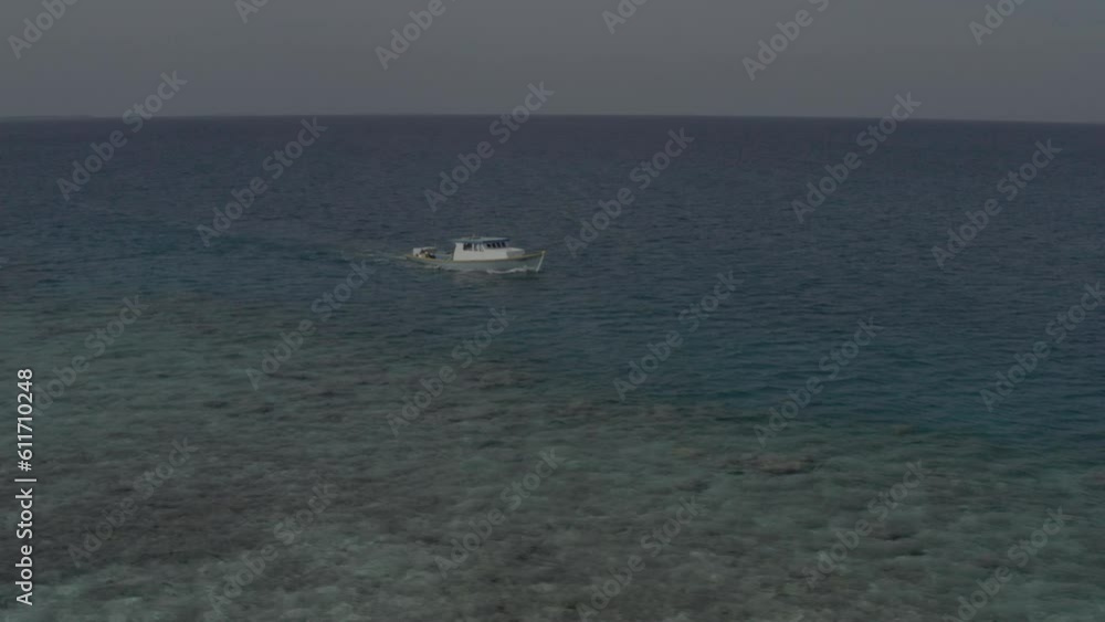 Aerial shot of a small white boat slowly sailing across the Indian Ocean in the Maldives with a small remote island in the background on a clear summer day. Footage without color correction. Aerial shot of a small white boat slowly sailing across the Indian Ocean in the Maldives with a small remote island in the background on a clear summer day. Footage without color correction.