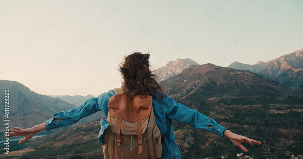 Young woman standing on top of mountain and victoriously raising hands up, looking far away - zen concept, freedom, adventure concept 