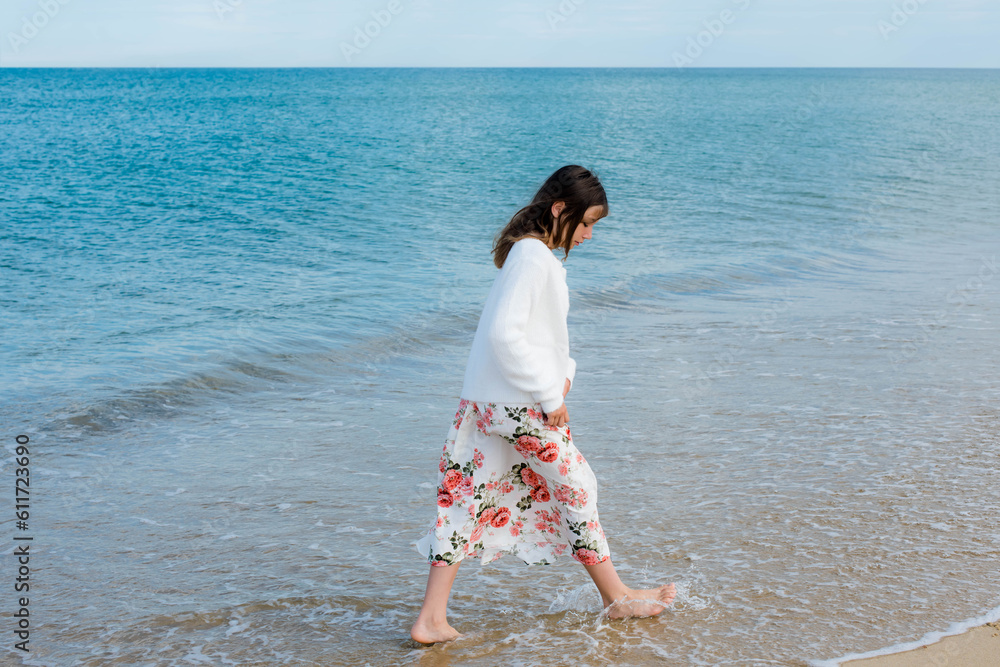 Beautiful fashionable young girl walking on the beach barefoot Beautiful fashionable young girl walking on the beach barefoot