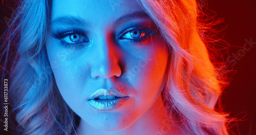 Sensual blonde caucasian girl with glowing makeup giving a tempting look in neon cyberpunk lights - nightlife concept close up portrait shot 