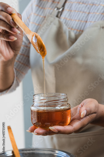 Female hands holding a bowl of bee honey and a wooden spoon. Close up. Elaboration of organic soap based on glycerin.