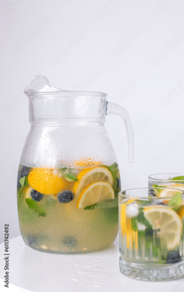 lemonade in a glass and a jug on a white background. Summer refreshing drink. Cold detox water with lemon lemonade in a glass and a jug on a white background. Summer refreshing drink. Cold detox water with lemon